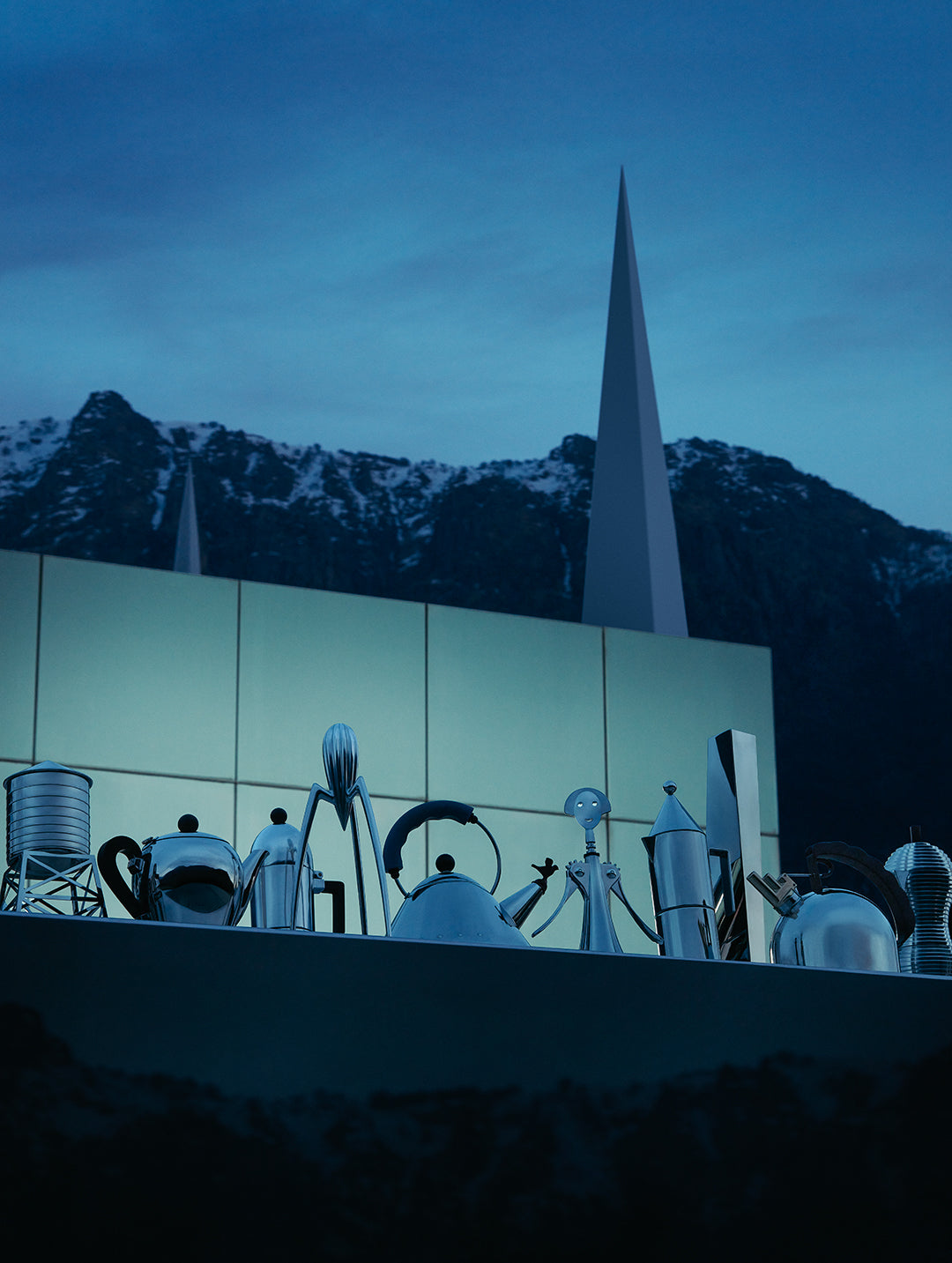 Futuristic metallic sculptures stand before a sleek building and snow-capped mountains under twilight skies.