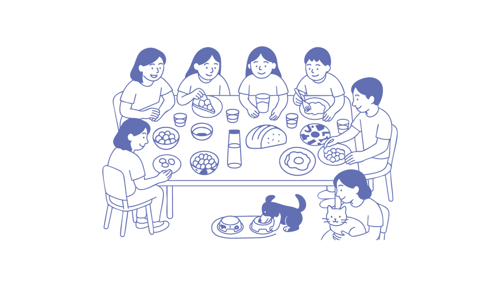 Six people share a warm meal at a dining table with pets nearby, embodying joyful cohabitation.