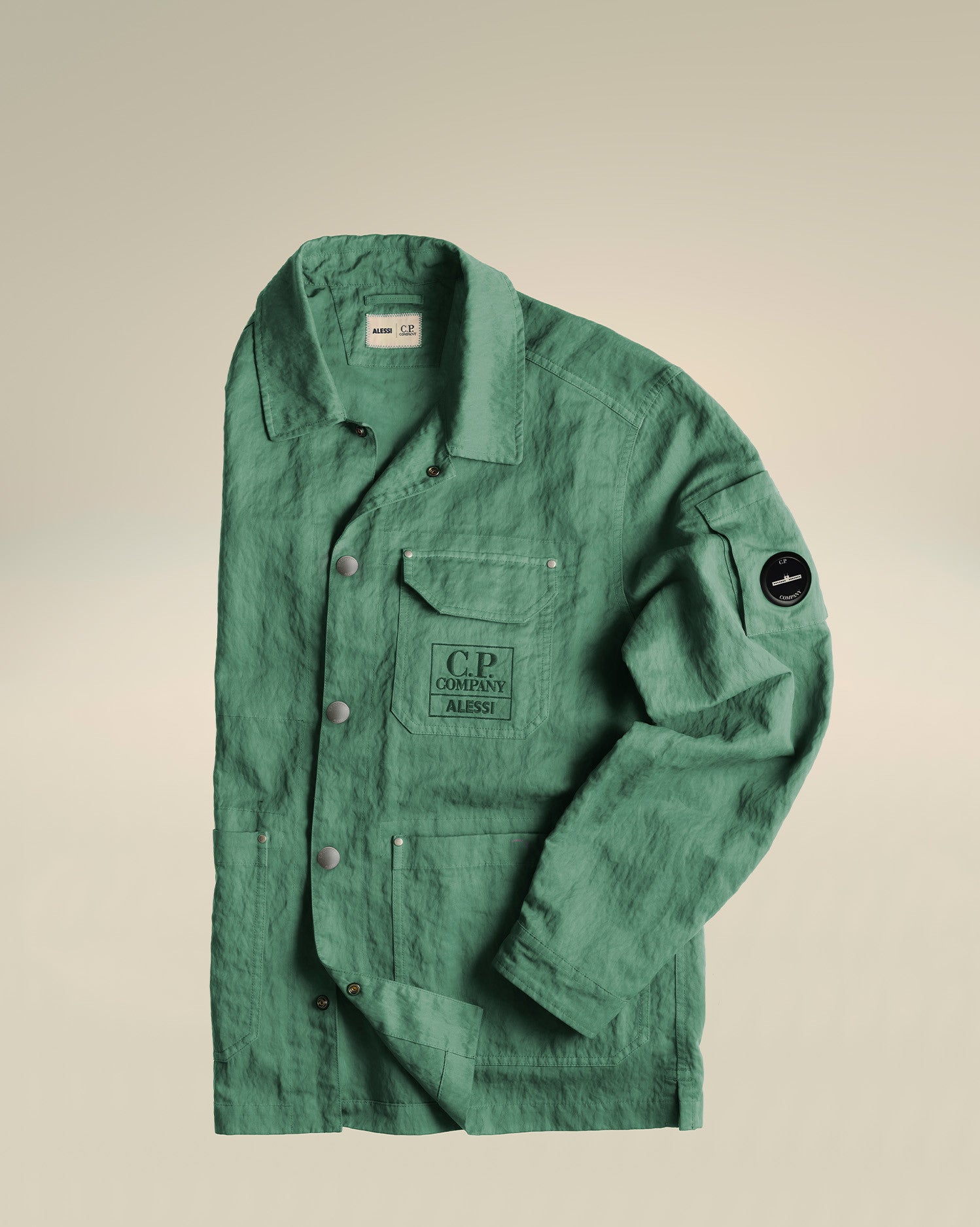 Green crinkled utility jacket by Alessi, with 'C.P. Company ALESSI' on a chest pocket, button-front, and a black 'C.P. Company' sleeve badge.