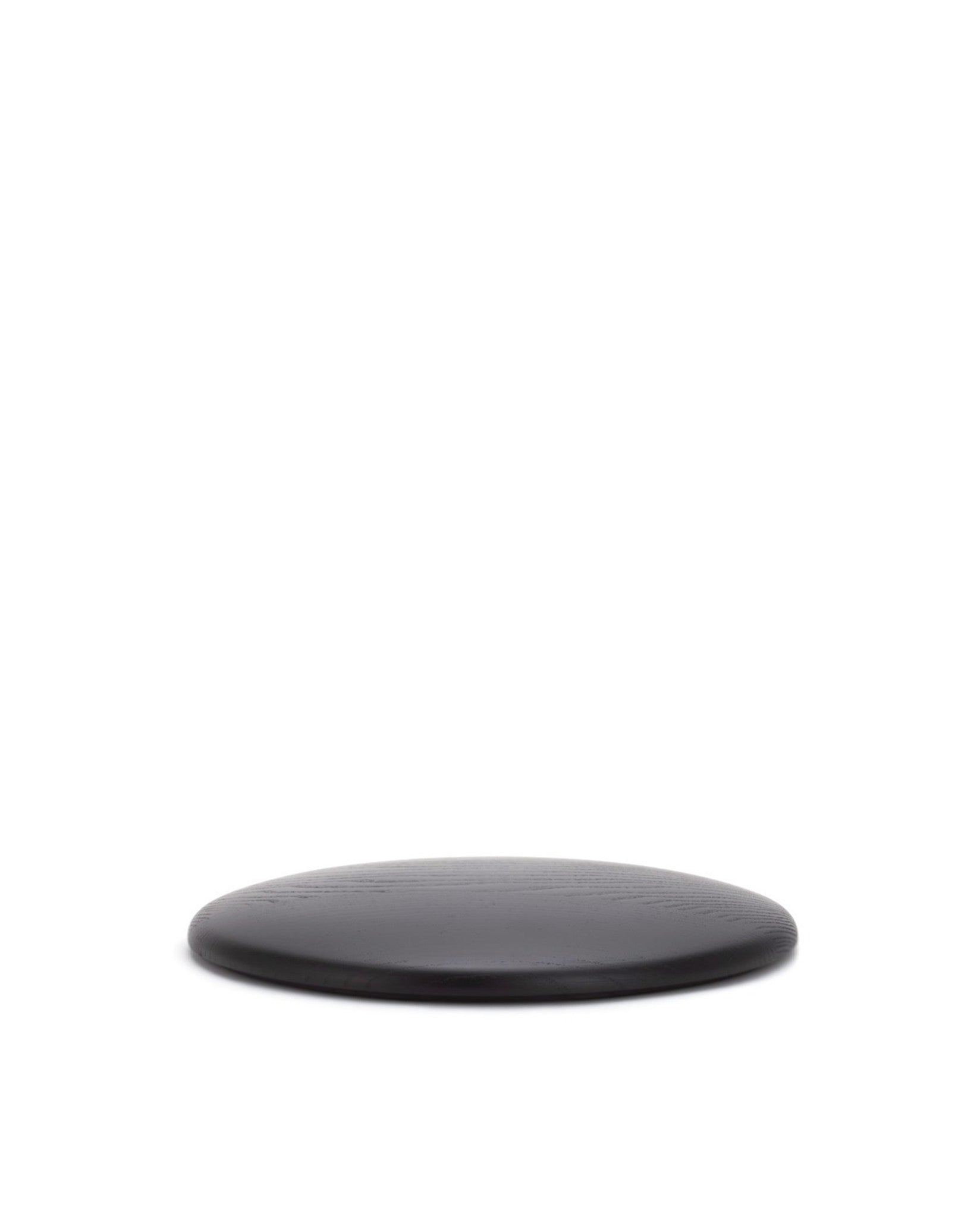 Dark round spare part by Alessi with visible wood grain texture, viewed at a low angle.