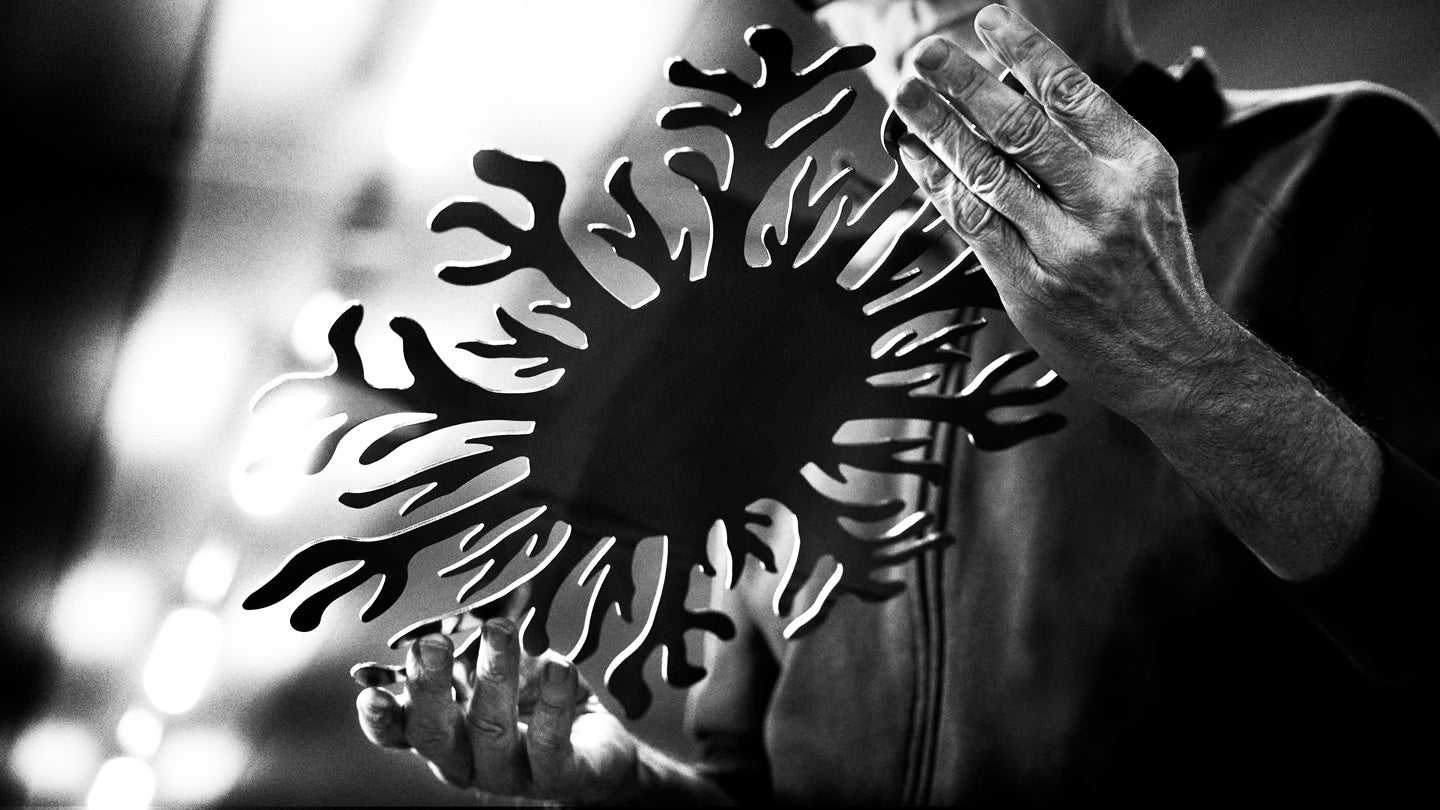 Hands holding intricate black metal snowflake cutout against bright, blurred background in black and white.